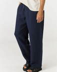 A person wearing loose, wide-leg navy pants with a drawstring waist, paired with a light cream t-shirt and black slide sandals, shown from the waist down on a plain white studio background.