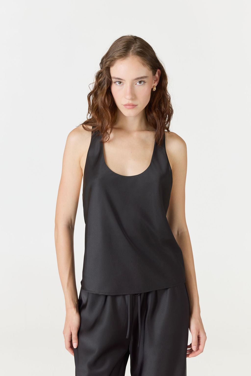 A woman modeling a black sleeveless scoop-neck top and matching black pants against a plain light gray studio background.
