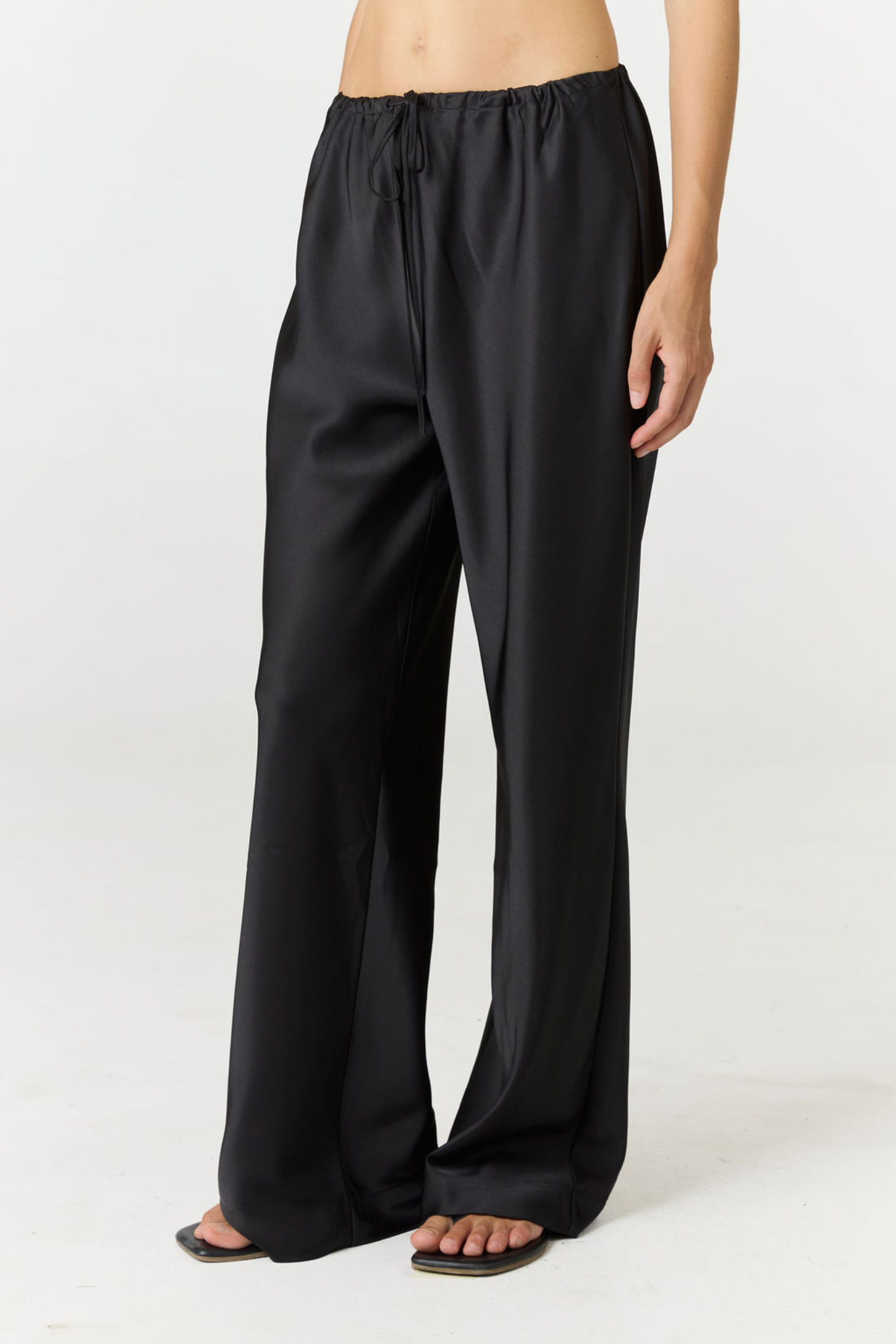 Black wide-leg drawstring pants worn by a model, shown from the waist down against a plain white studio background.