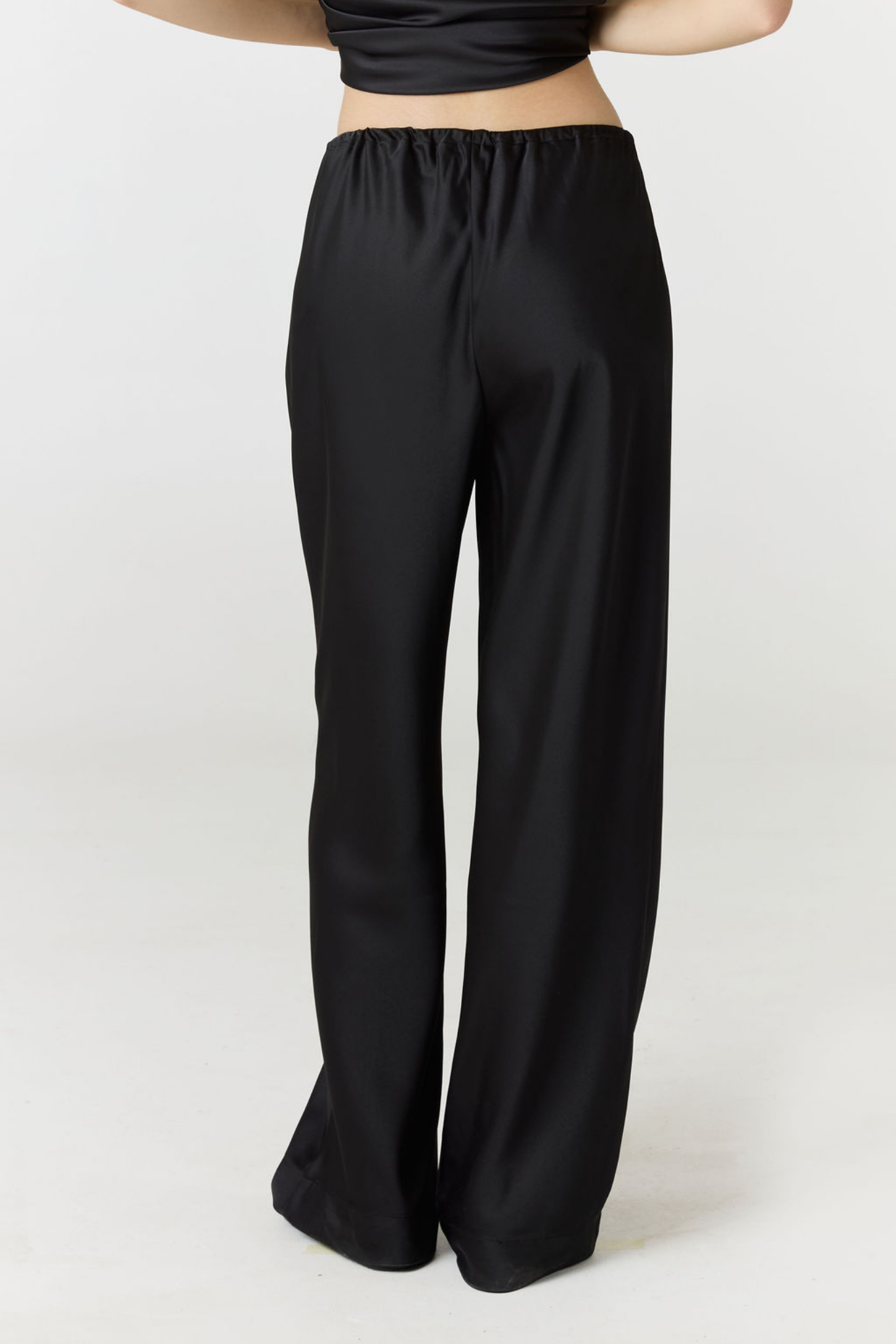 Black wide-leg pants with an elastic waistband, shown on a model from the back against a light gray studio background.