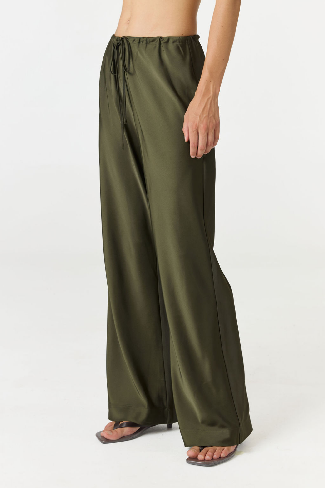 A person wearing wide-leg olive green satin or silky drawstring pants, shown from the waist down against a plain light gray studio background.