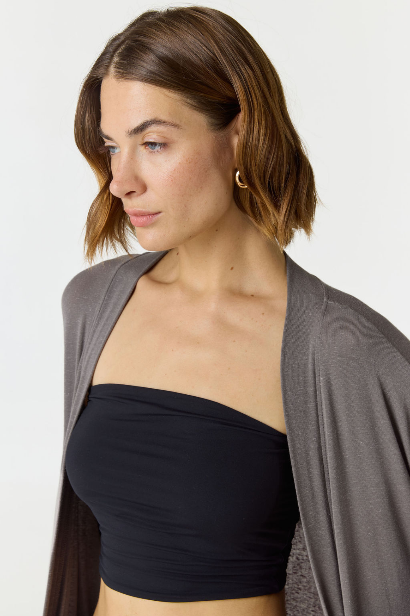 A woman wearing a black strapless bandeau top and a draped gray cardigan, shown from the chest up against a plain light background.