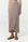 A model wearing a taupe wrap midi skirt with an asymmetrical hem and black strappy flat sandals, shown from the waist down on a white studio background.